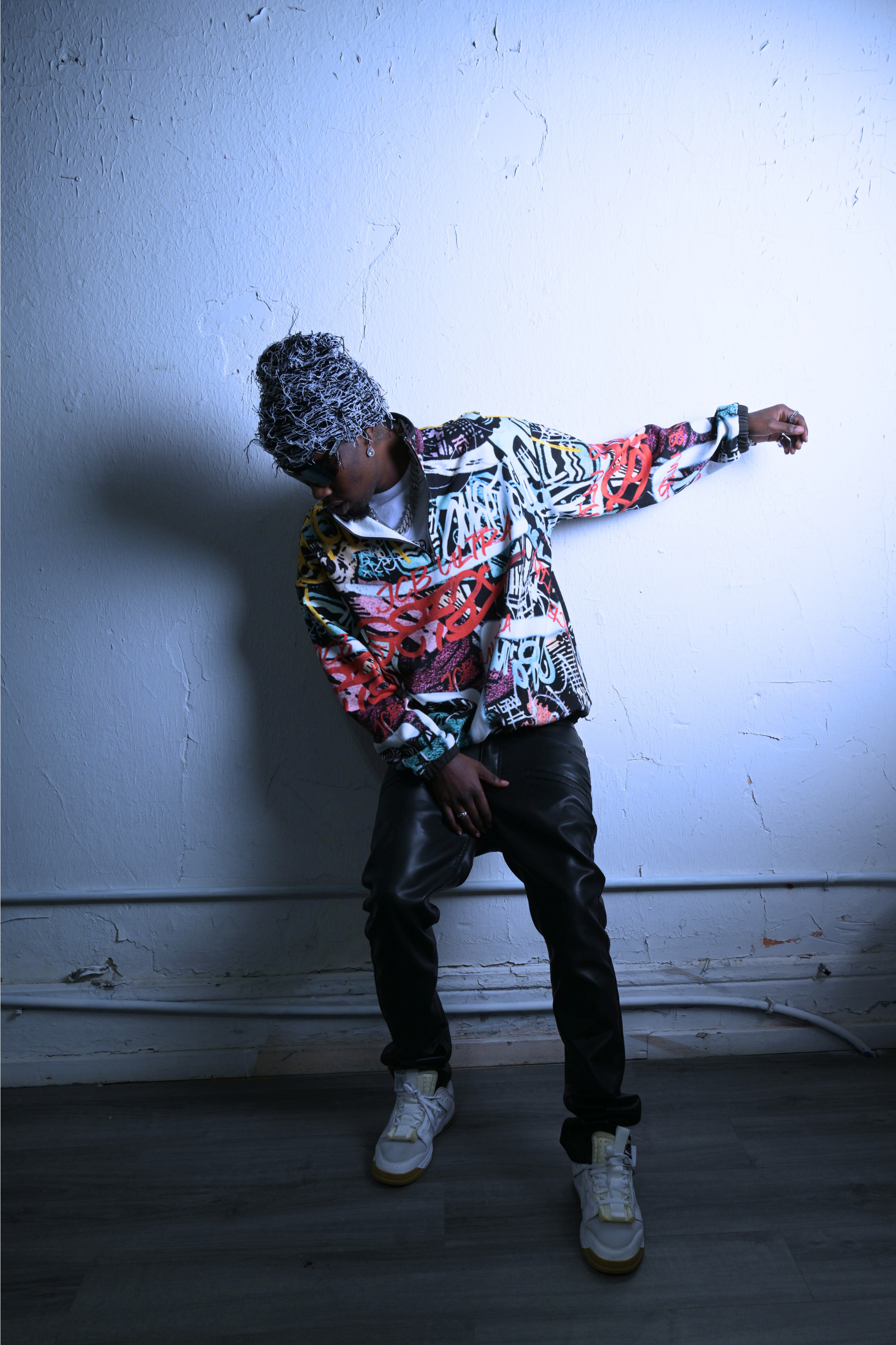 A picture of a black male model showing off the city chaos pullover by JCB ULTRA. A streetwear piece with a exclusive JCB ULTRA graffiti print. He is shown leaning to the side in a dramatic pose. 