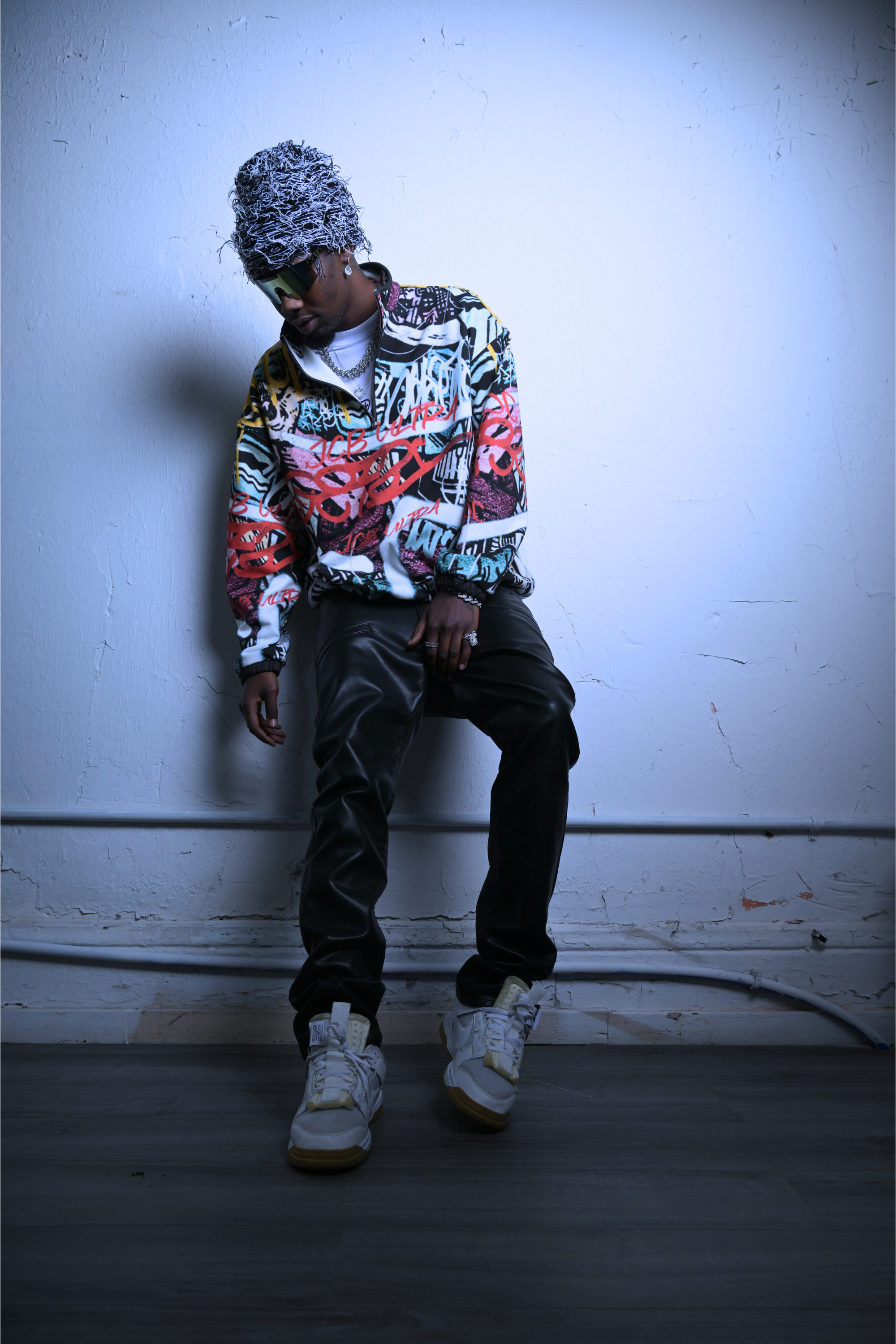 A black male model for JCB ULTRA shown leaning against a wall while wearing the city chaos pullover by JCB ULTRA.